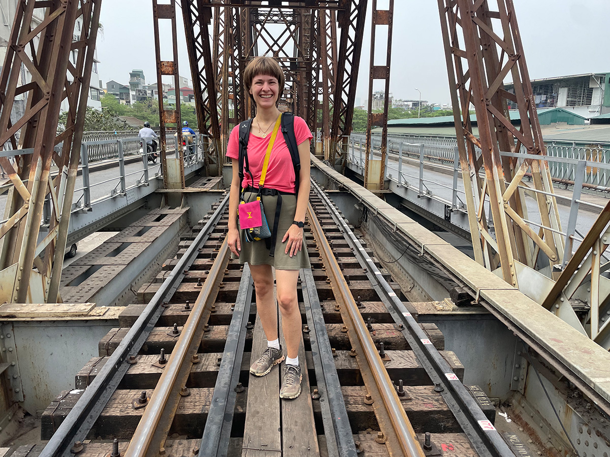Sustainable insider tips from the Free Walking Tour in Hanoi Eine Person lächelt auf einer alten Eisenbahnbrücke, umgeben von Metallkonstruktionen und Schienen.
