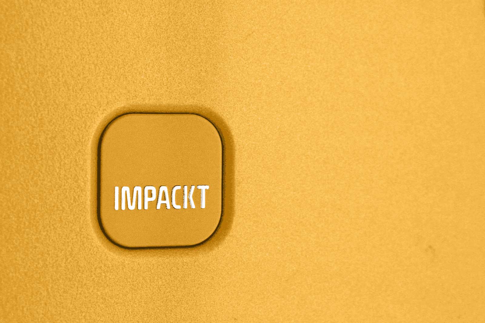 Detailaufnahme eines gelben Objekts mit der Aufschrift 'IMPACKT' in Weiß Nahaufnahme eines gelben Gegenstands mit hervorstehendem Quadrat und weißem Text 'IMPACKT'