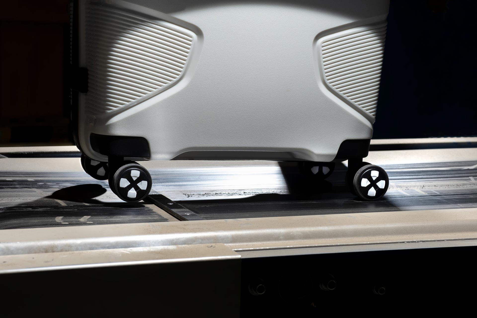 Moderner Reisekoffer mit stabilen Rollen auf einem Förderband Nahaufnahme eines weißen Reisekoffers mit fünf Rollen auf einem Transportband