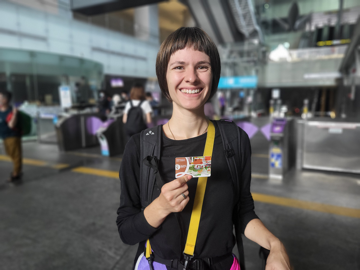 Discover Taiwan by public transport: the best tips from bus to train Eine lächelnde Person hält eine Fahrkarte in einem modernen Bahnhof in der Hand.