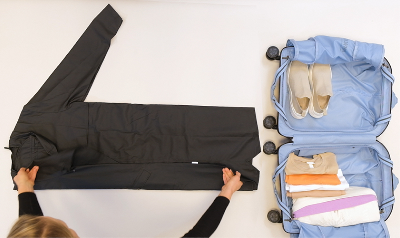 Effektives Packen: Kleidung und Schuhe im Koffer organisiert Eine Person faltet eine Jacke neben einem offenem Koffer voller gefalteter Kleidung und Schuhe