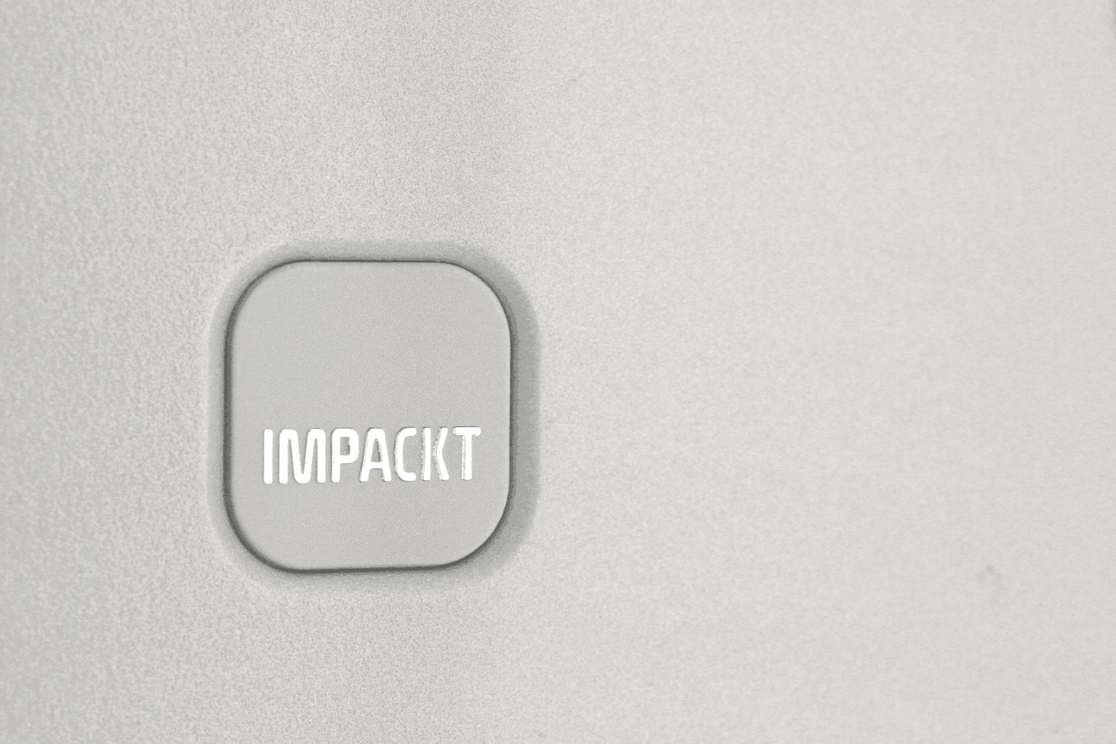 Graues Quadrat auf Betonwand mit der Aufschrift 'IMPACKT' Nahaufnahme eines grauen Quadrats auf einer glatten, hellgrauen Oberfläche mit der Aufschrift 'IMPACKT'