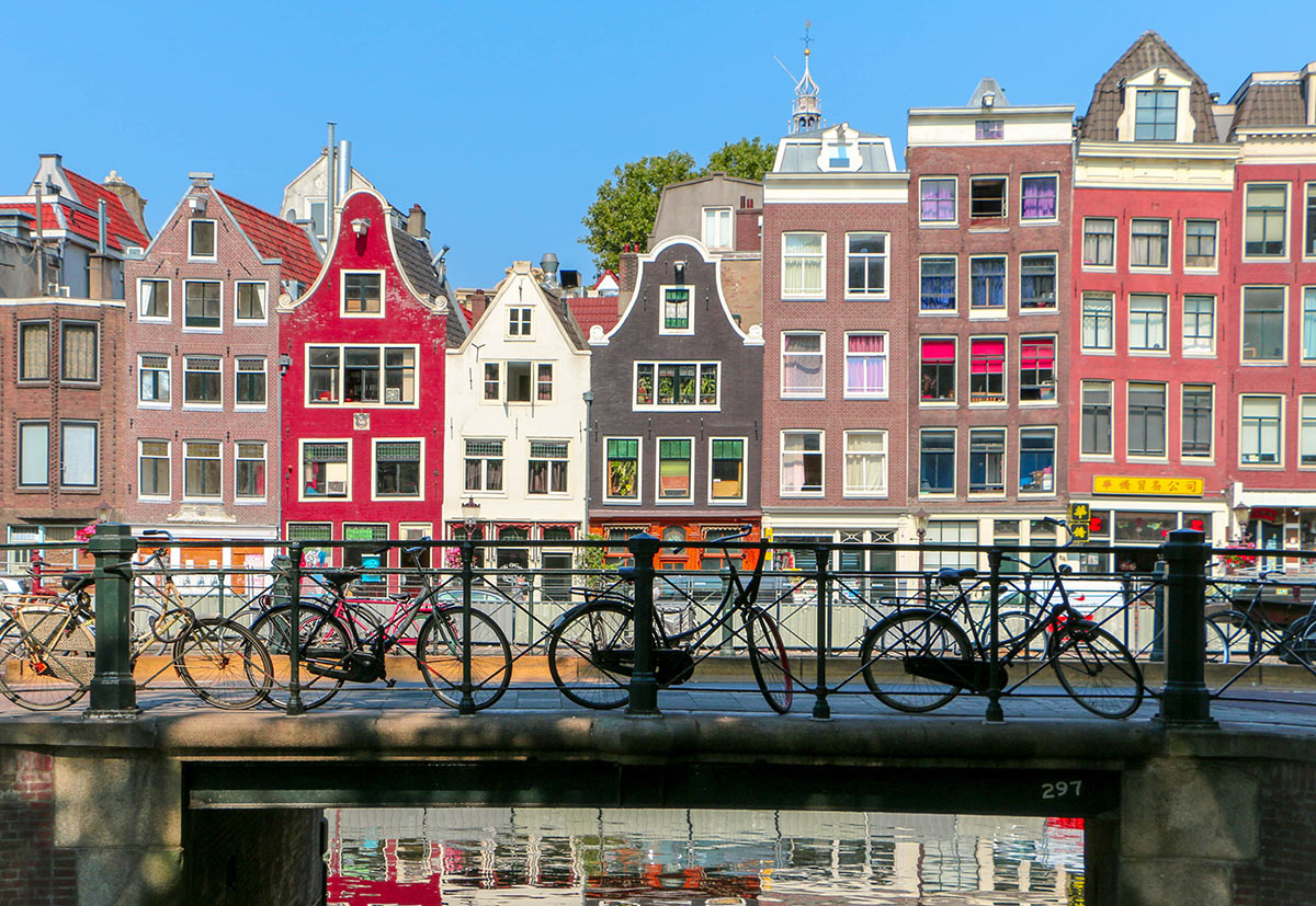 Visit hot spots in an environmentally friendly way: Amsterdam Fahrräder stehen auf einer Brücke mit Blick auf bunte historische Häuser in Amsterdam bei klarem Himmel