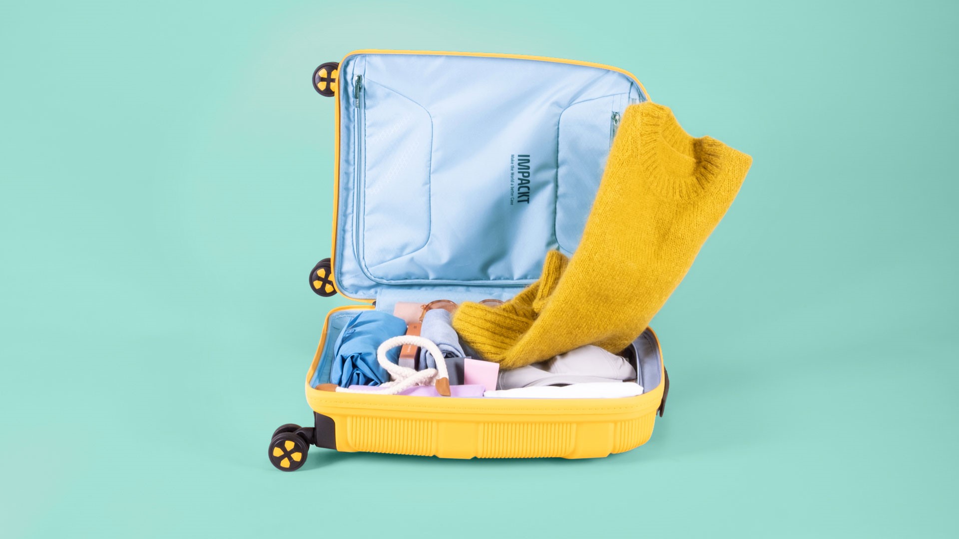 Offener gelber Koffer mit Kleidung und Accessoires auf türkisfarbenem Hintergrund Ein geöffneter gelber Koffer, der mit Kleidung und Accessoires, darunter ein gelber Pullover, auf einem türkisfarbenen Hintergrund liegt.