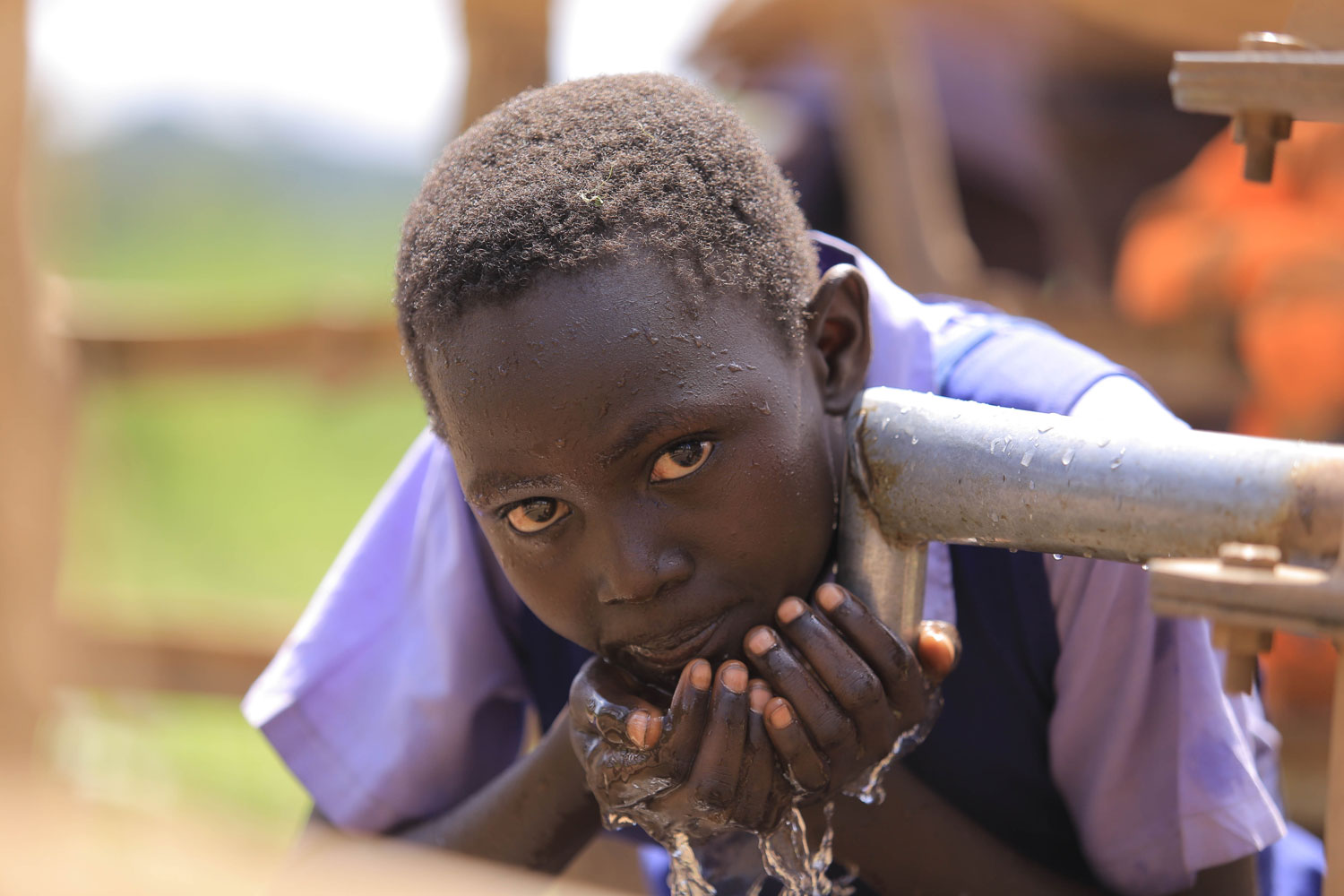 Kind trinkt Wasser aus einer frisch angezapften Quelle Ein Kind in Schuluniform trinkt Wasser aus einem Rohr, umgeben von natürlicher Umgebung